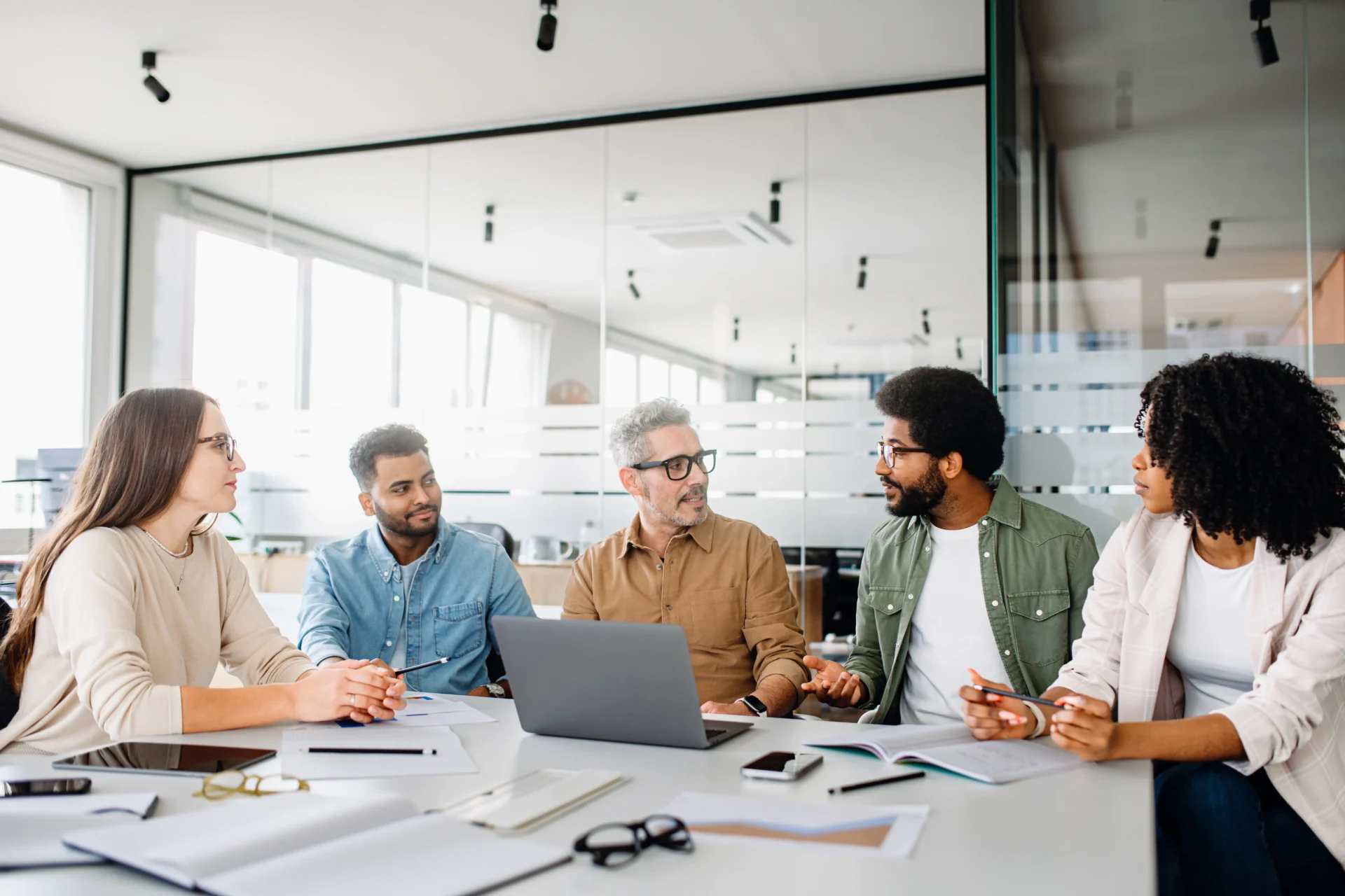 Four professionals discussing ideas around a laptop in a bright office.